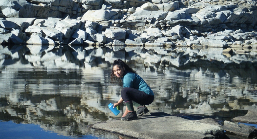 A person kneels on rock near a body of water that reflects the rocks on the shore. 